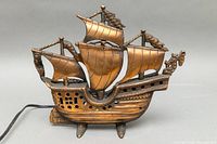 Front view of cast iron pirate ship lamp showing detailed sails and hull design, bronze color