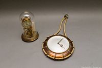 Photo showing both the Kundo domed mantle clock under a glass dome on the left and the Phinney Walker wall clock on the right side, placed on a flat surface.