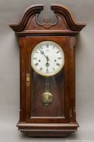 Full view of wooden Sligh pendulum wall clock with glass front door and carved top.