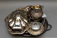 Overall view of vintage silver plated serving set including covered butter dish, creamer, sugar bowl and ornate trays with tarnishing and light scratches