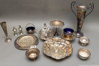 Photo showing entire collection of eleven silver plated items including the tall trumpet vase, salt and pepper shakers, condiment bowls with blue glass inserts, pedestal compote, divided serving dish, and smaller bowls arranged on table.