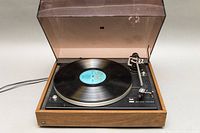 Vintage Dual 502 belt drive stereo turntable with record spinning, housed in wooden base with clear plastic dust cover.