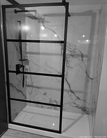 Marble-patterned white acrylic shower wall system with black-framed glass enclosure