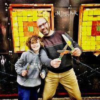 Two people holding neon-painted axes in front of wooden target board