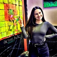 Individual holding painted throwing axe in front of neon-painted wooden target board