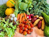 Variety of vegetables including yellow squash, white mushrooms, carrots, radishes, cherry tomatoes, potatoes, zucchini, kale and lettuce displayed on wooden surface