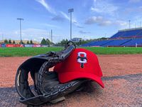 Red Ottawa Titans cap and black baseball glove placed on the field near home plate