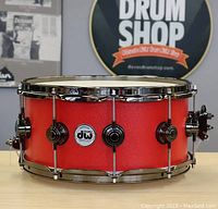 Front view of DW snare drum on table with red sparkle shell, chrome hardware, Dave’s Drum Shop sign in background
