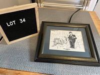 Framed black and white print by Bill Day laid flat on a gray cloth with a lot number sign next to it showing that it is lot 34.