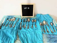 Three separate replacement sets of Birks Regency plate cutlery laid out on blue cloth showing the Queen Mary pattern handles and visible tarnish.