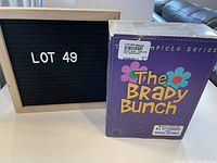 Photo showing the front of The Brady Bunch boxed set for the complete series, purple with colorful flowers and text.
