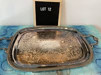 Front angled top view of the rectangular silverplate serving tray with two ornate handles, showing tarnish and etched design.