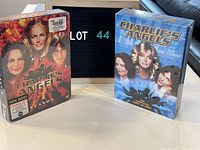 Two sealed DVD box sets of Charlie's Angels Seasons 1 and 2 positioned upright with a lot number sign behind them showing lot 44.
