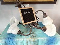 Traditional five light chandelier with curled arms in charcoal grey metal finish with frosted glass bell-shaped shades, displayed on a fabric surface.