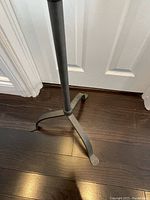 Close-up photo of the dark grey metal tripod legs of the floor lamp standing on a dark wood floor.