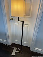 Full view of floor lamp showing door background, silver base, black vertical arm, and beige lampshade.