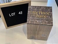 Front and top angled view of the boxed DVD set shaped like a small wooden house with 'Little House on the Prairie THE COMPLETE SERIES' text on top.