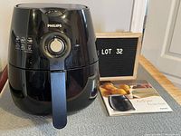 Front view of black Philips air fryer sitting on a countertop with the recipe book beside it.