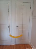 Full view of one swing hanging from a door showing the yellow plastic seat with rope and chain support