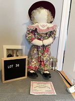 Front view of the vintage "Time Out Kid" cloth doll with a maroon hat, curly blonde hair, floral outfit, white collar, and patent leather shoes. Certificate of authenticity placed on the floor in front of the doll.