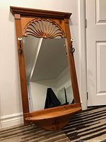 Full view of vintage wooden hallway mirror showing carved fan design, shelf, and hooks on sides.