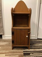 Front view of the vintage pine country cupboard showing the pointed top, open shelf, and closed cabinet door with white knob and black hinges.