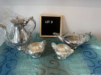 Full set of 4 items: coffee pot, tea pot, creamer, and sugar bowl displayed on a blue patterned cloth with a label board behind them.