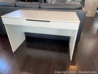 White modern writing desk placed on dark hardwood floor, showing front with drawer closed.