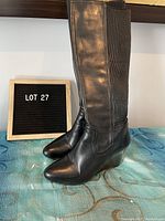 Side view of pair of black leather knee-high boots showing smooth front leather and ribbed back panel with wedge heel