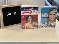 Full view of both boxed TV series sets: Wonder Woman and The Bionic Woman, along with lot board.