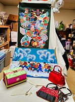 Full lot view showing two paintings on fabric, sewing basket with threads, red cloth purse, and two foldable purses.