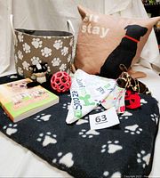 Photo shows the full lot including paw print dog bed, three dog toys (red ball, giraffe, ladybug), the book 'You & Your Puppy', dog toy storage basket with paw prints, three dog neckerchiefs on the bed, and decorative pillow with black dog silhouette and "Sit Stay" text.