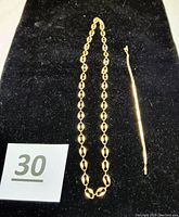 Full lot view showing gold necklace with oval-shaped links and the slender bracelet on black background.