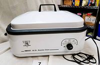 Full view of white and black Nesco electric roaster oven with lid and handles.