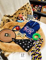 Overview photo showing the fuzzy dog bed, black fleece blanket, various dog toys including frisbee, plush toy, Kong ball, chew ring, the dog jacket, and black paw print bandana.