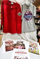 Two large shirts displayed: red long sleeve Majestic shirt with 2008 World Series patch and grey short sleeve Majestic World Series Champions 2008 graphic shirt. Four Philadelphia Inquirer posters arranged below them.
