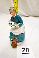 Side view of the Royal Doulton lady figurine with ruler showing height about 7 inches, lady pouring milk to cat.