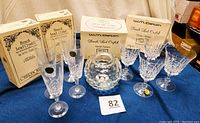 Eight clear crystal glasses including four goblets and four parfait/sour glasses in original WM Dalton boxes with labels visible, plus a vintage Fostoria votive candle holder, displayed on a table.