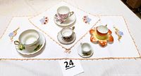 Full view of five floral tea cup and saucer sets placed on two embroidered table runners with peach-colored edges