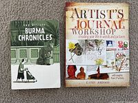Front covers of 'Artist's Journal Workshop' and 'Burma Chronicles' laid flat on a carpeted floor.
