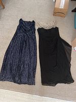 Photo showing the two gowns laid flat on carpet floor, navy blue sequin gown on left, black gown with sequined sheer yoke on right