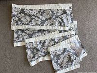 Set of four fabric window valances laid flat on carpet showing pattern and white trim.