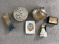 6 miscellaneous collectible items shown together on carpet background, including an Irish musical statue, Roman bride and groom figurine, silver plated condiment set, signed vase, small box, and lidded dish.