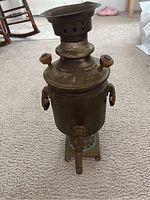 Front view of antique brass samovar canister showing spigot, handles, and base.