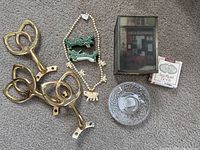 Lot items on carpet background including three brass fan blades, two green dragon figurines, a white elephant bead necklace, a clear glass Orrefors discus candle holder, a small box candle holder, a Logan burger pin, and Sweetheart tie-on collectible box.