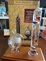 AcuRite Galileo Thermometer with original box in background, showing detailed design and labeled box information.