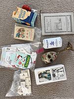Top view of all items in lot laid on carpet including breast pump box, pin cushion, ceramic mask, clothing in plastic bags, figurine in box and other small packages