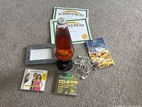 Photo showing lava lamp, two achievement certificates, marble picture frame, Heartbreakers CD, CD-R disc, Magic Bullet recipe book, and Apple wired earphones all laid out on carpeted floor.