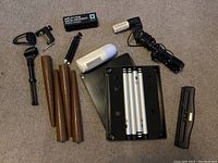 Full assortment of stand legs, clamps, light bulb, small electronic device, mounting rods and punch tool spread on floor.