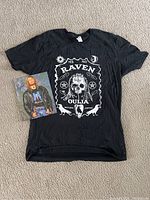 Full view of black XL T-shirt with white 'Raven Ouija' skull graphic and autographed 8x10 photo of Raven.